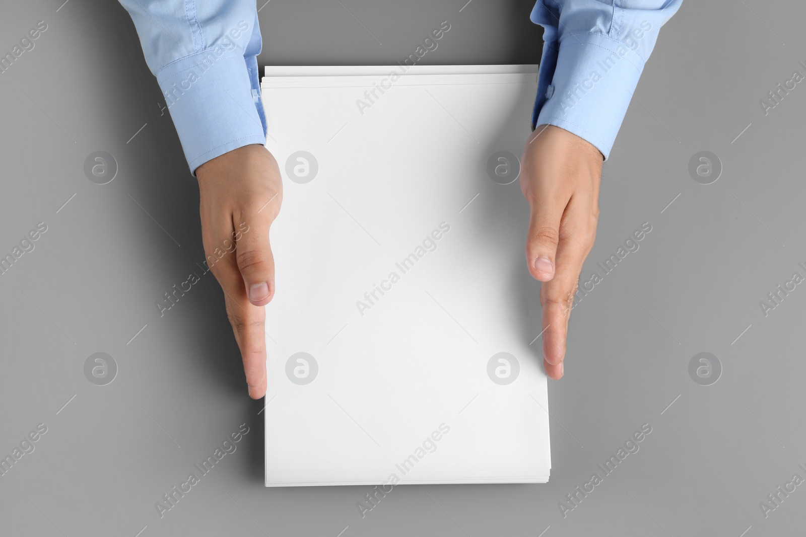 Photo of Man holding blank paper sheets for brochure at grey table, top view. Mock up