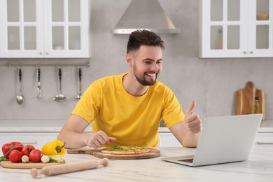 Smiling man making pizza while watching cooking online course in kitchen. Time for hobby