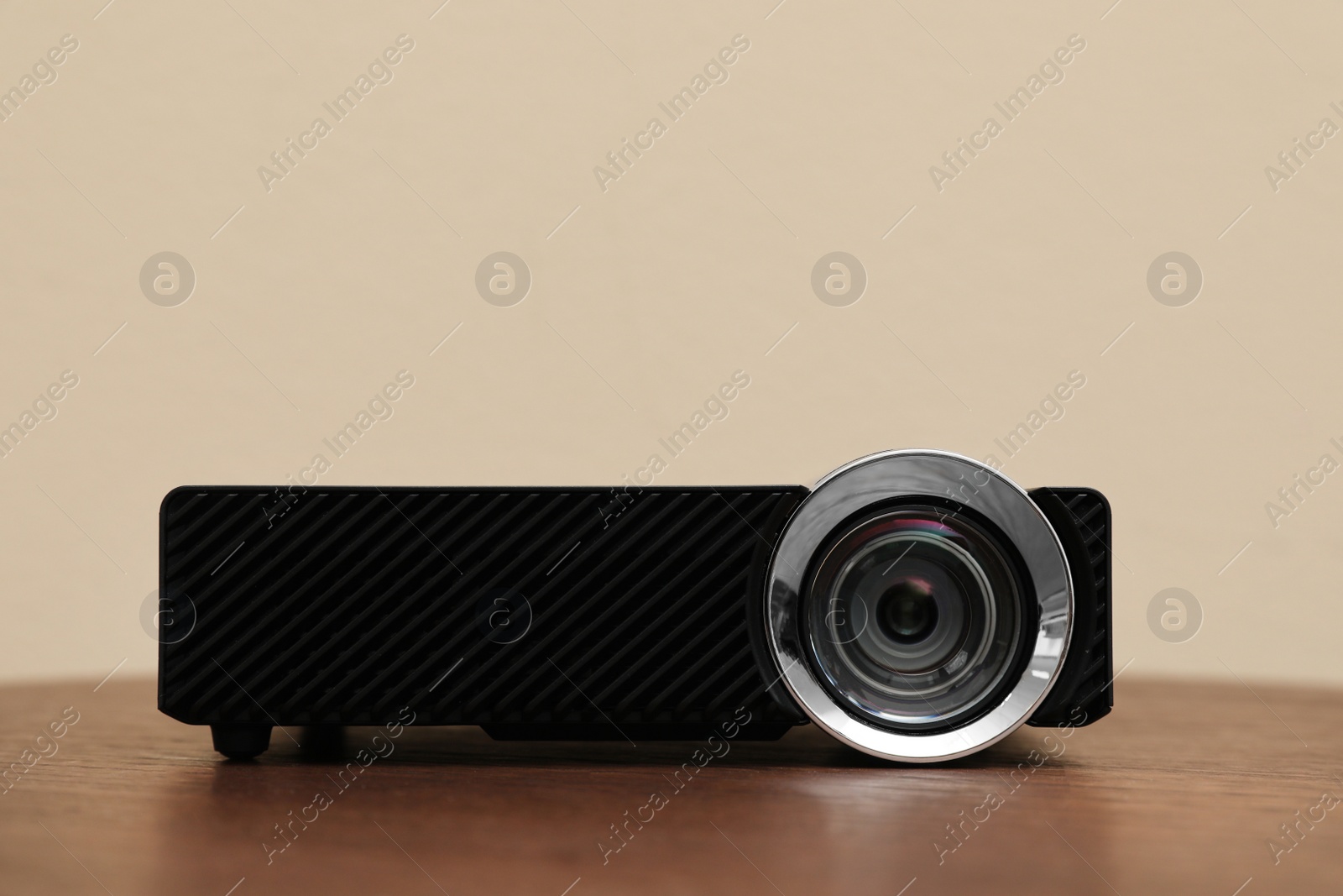 Photo of Modern video projector on wooden table against beige background