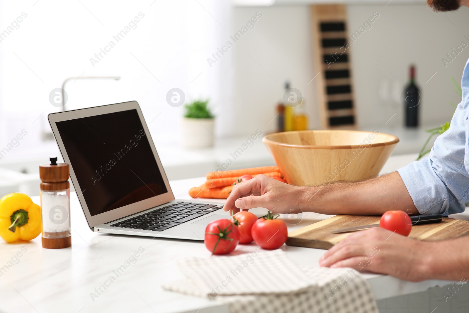 Photo of Man making dinner while watching online cooking course via laptop in kitchen, closeup