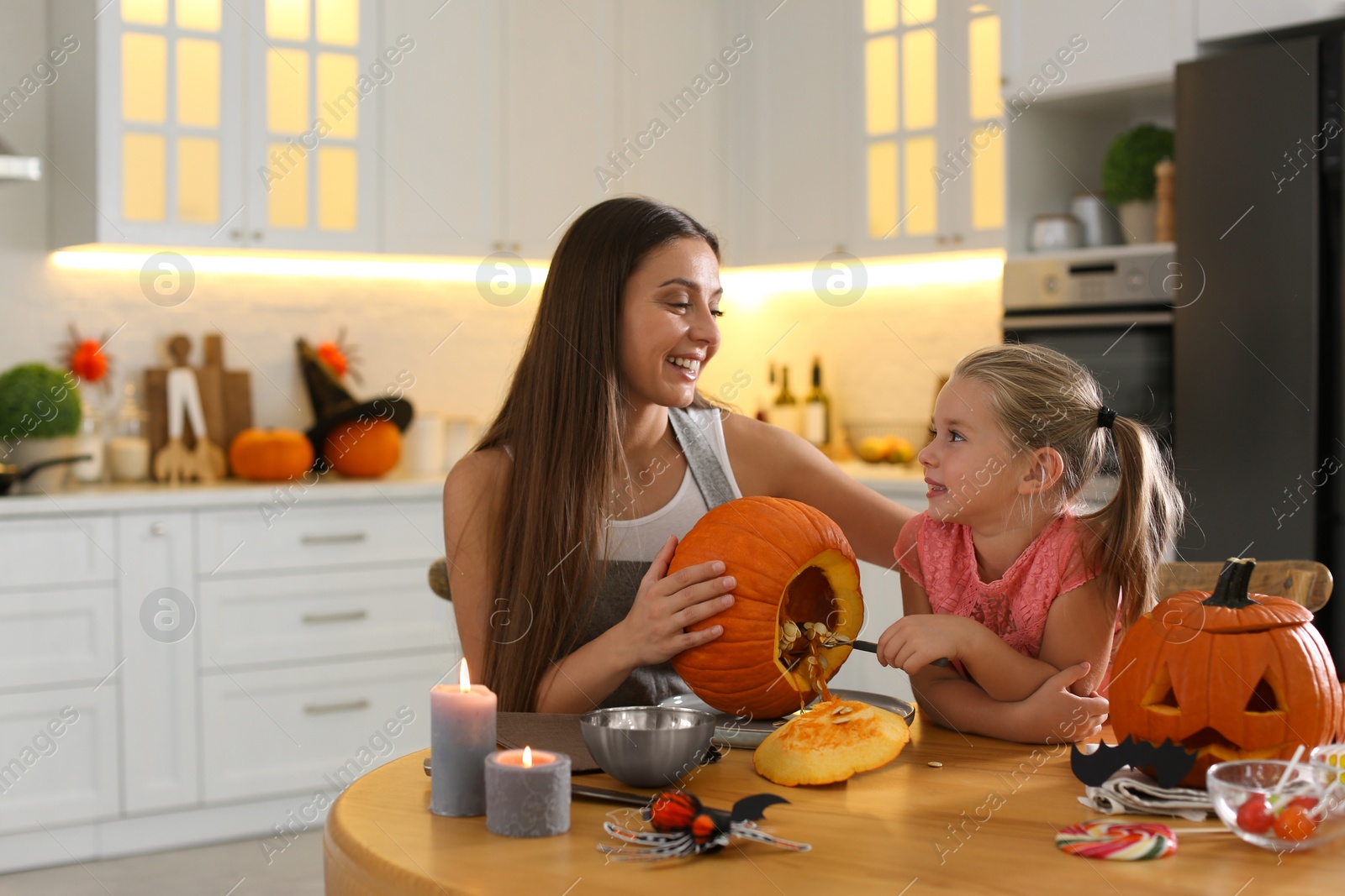 Photo of Mother and daughter making pumpkin jack o'lantern at table in kitchen. Halloween celebration