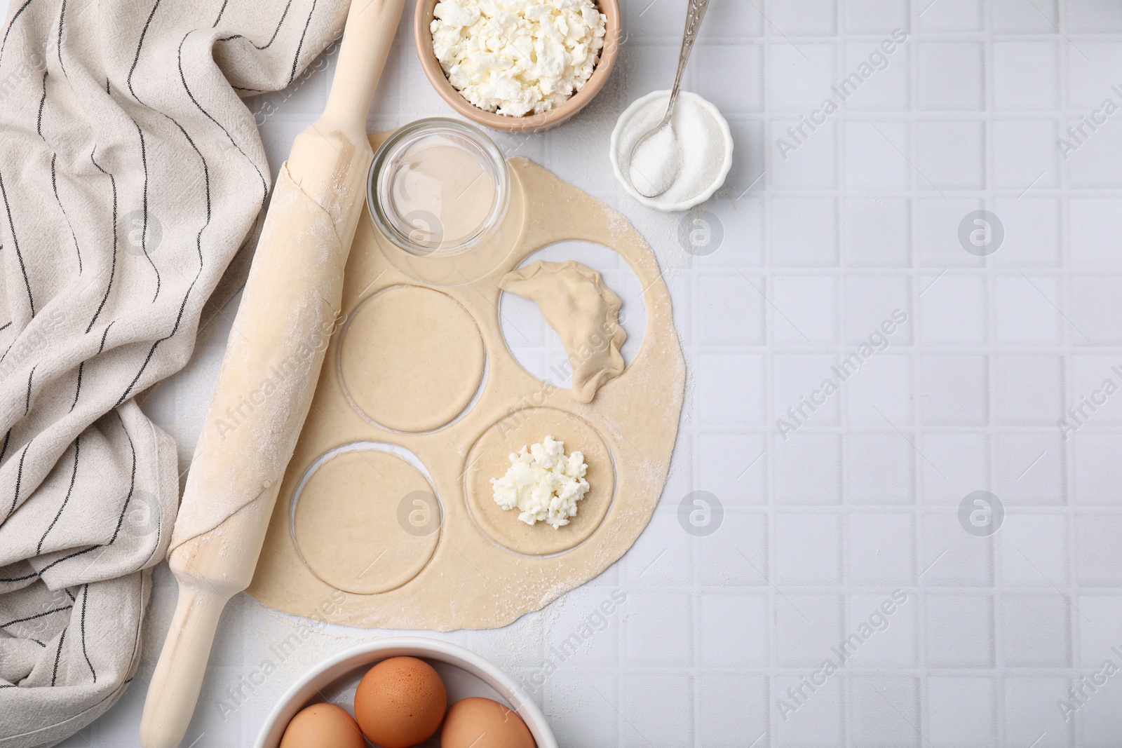 Photo of Process of making dumplings (varenyky) with cottage cheese. Raw dough and ingredients on white tiled table, flat lay. Space for text