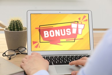 Image of Bonus gaining. Man using laptop at table, closeup. Illustration of gift box and word on device screen
