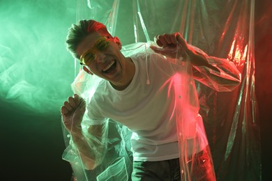 Stylish young man wearing clear coat and glasses in neon lights