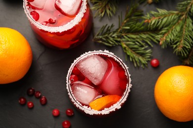 Photo of Tasty cranberry cocktail with ice cubes in glasses on dark gray table, flat lay