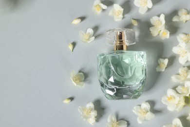 Photo of Aromatic perfume in bottle and beautiful jasmine flowers on grey background, flat lay. Space for text