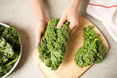 Woman holding fresh kale leaves over light grey table, top view