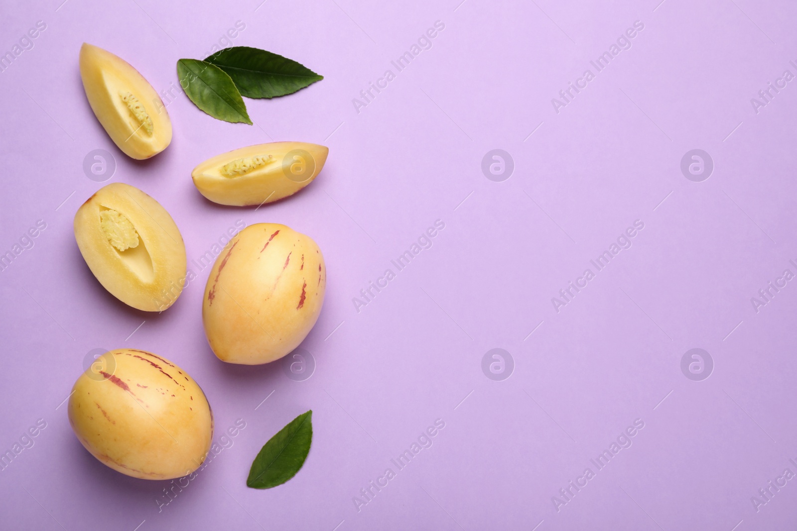 Photo of Whole and cut pepino melons with green leaves on violet background, flat lay. Space for text