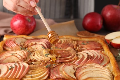 Photo of Woman adding honey to freshly baked apple pie at table, closeup