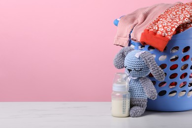 Photo of Laundry basket with baby clothes near crochet toy and bottle on white marble table, space for text