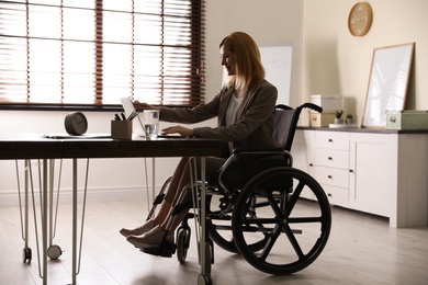 Woman in wheelchair working with laptop at table indoors