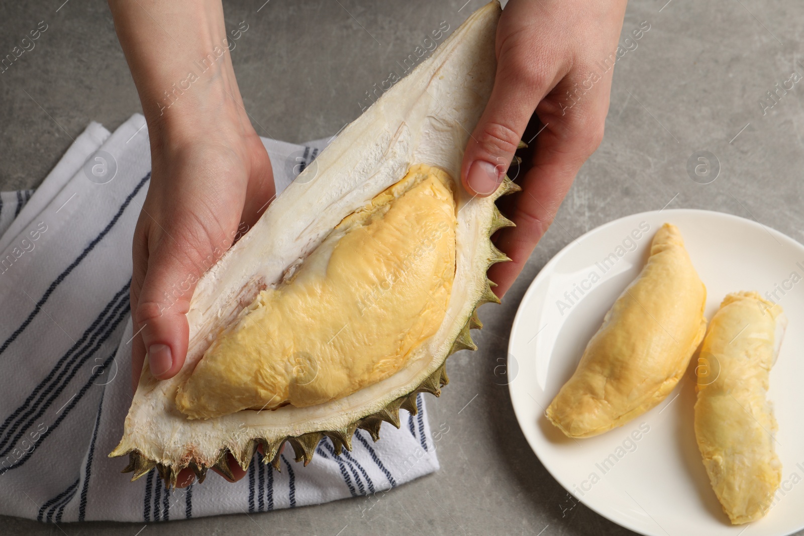 Photo of Woman holding piece of ripe durian over grey table, top view