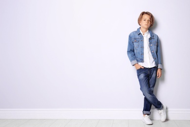 Cute little boy in casual outfit near white wall. Space for text