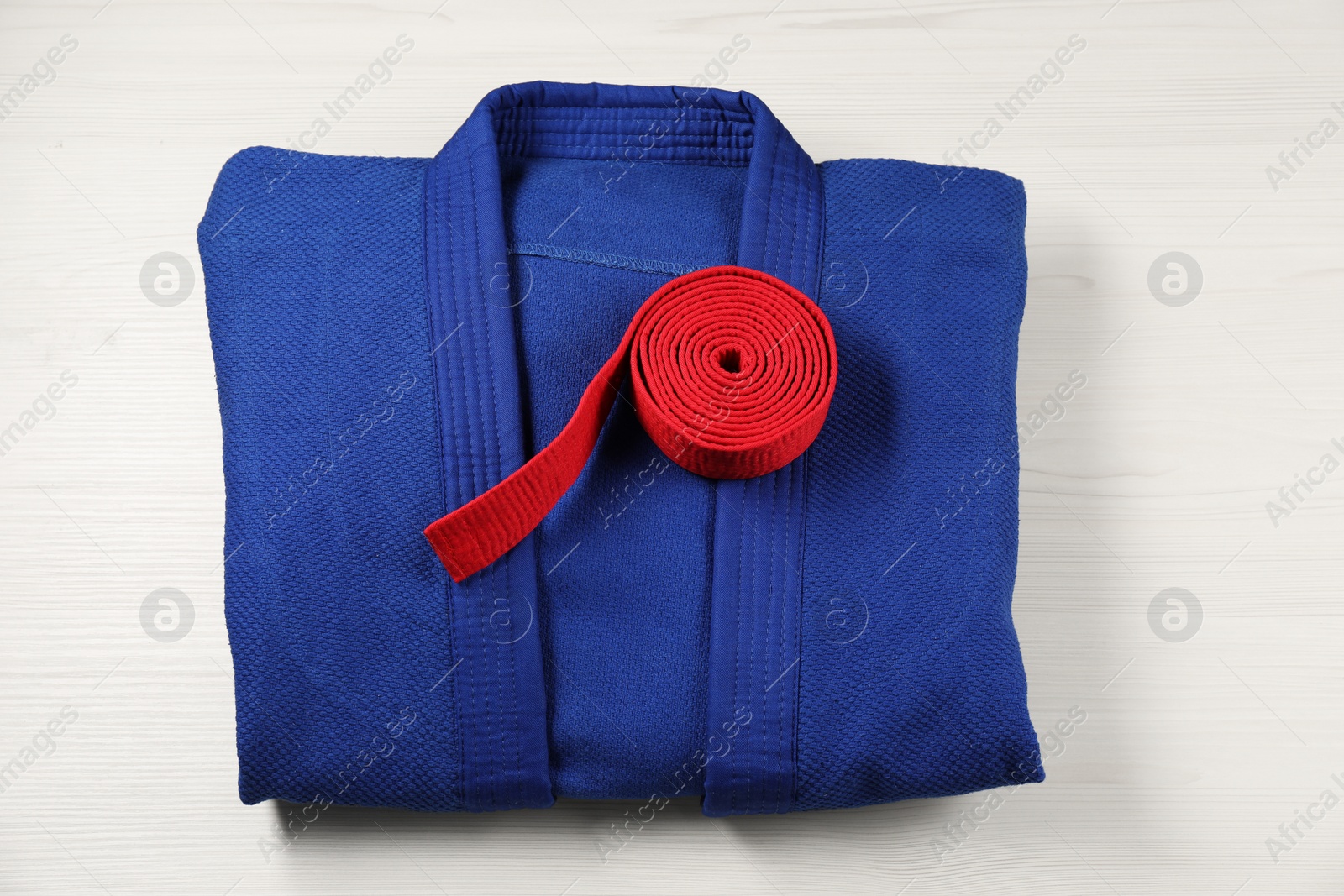 Photo of Red karate belt and blue kimono on wooden background, top view