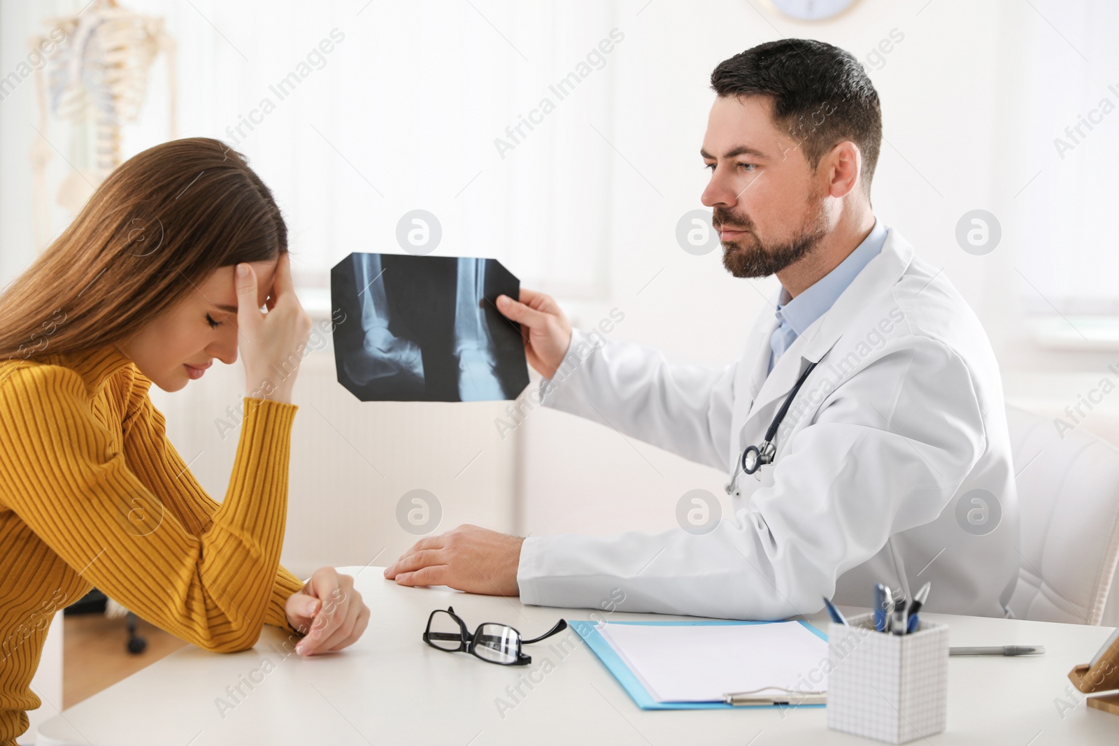 Photo of Orthopedist showing X-ray picture to patient at table in clinic