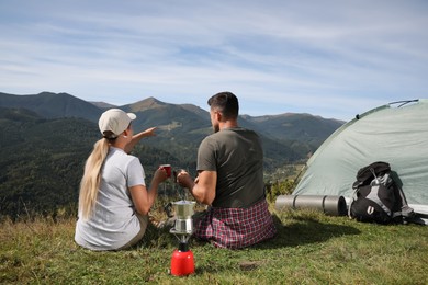 Photo of Couple with drinks enjoying mountain landscape near camping tent, back view
