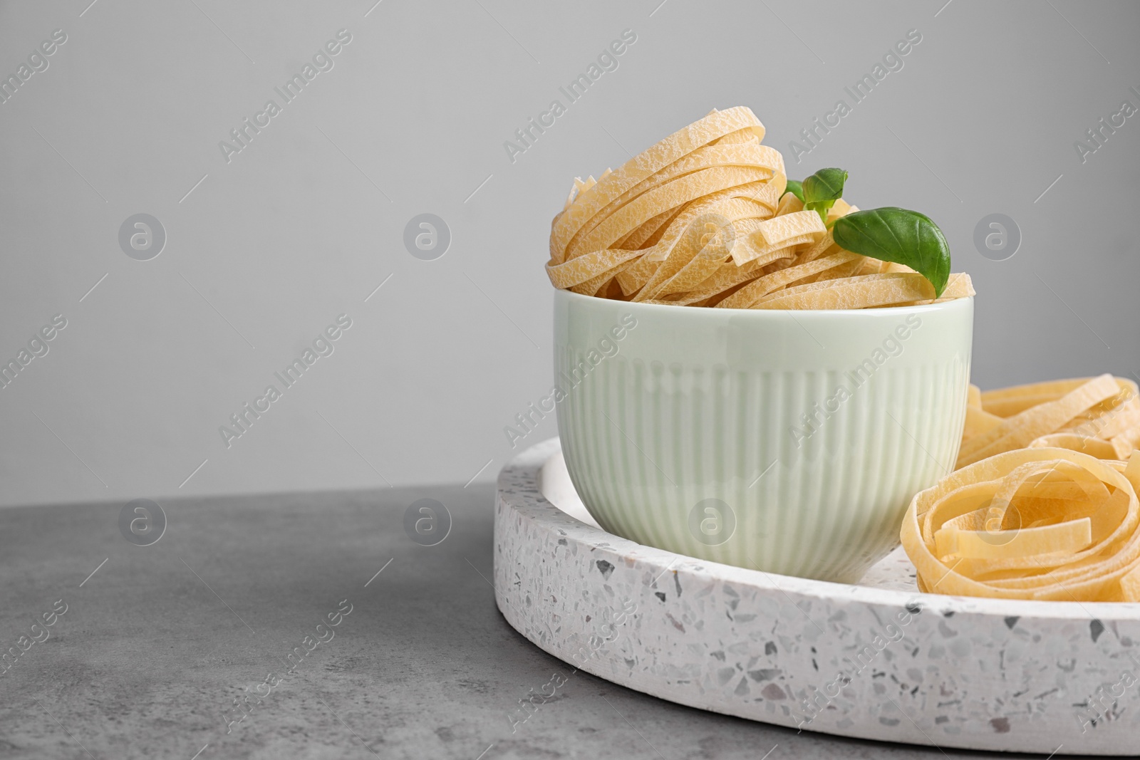 Photo of Uncooked tagliatelle pasta on table against grey background. Space for text