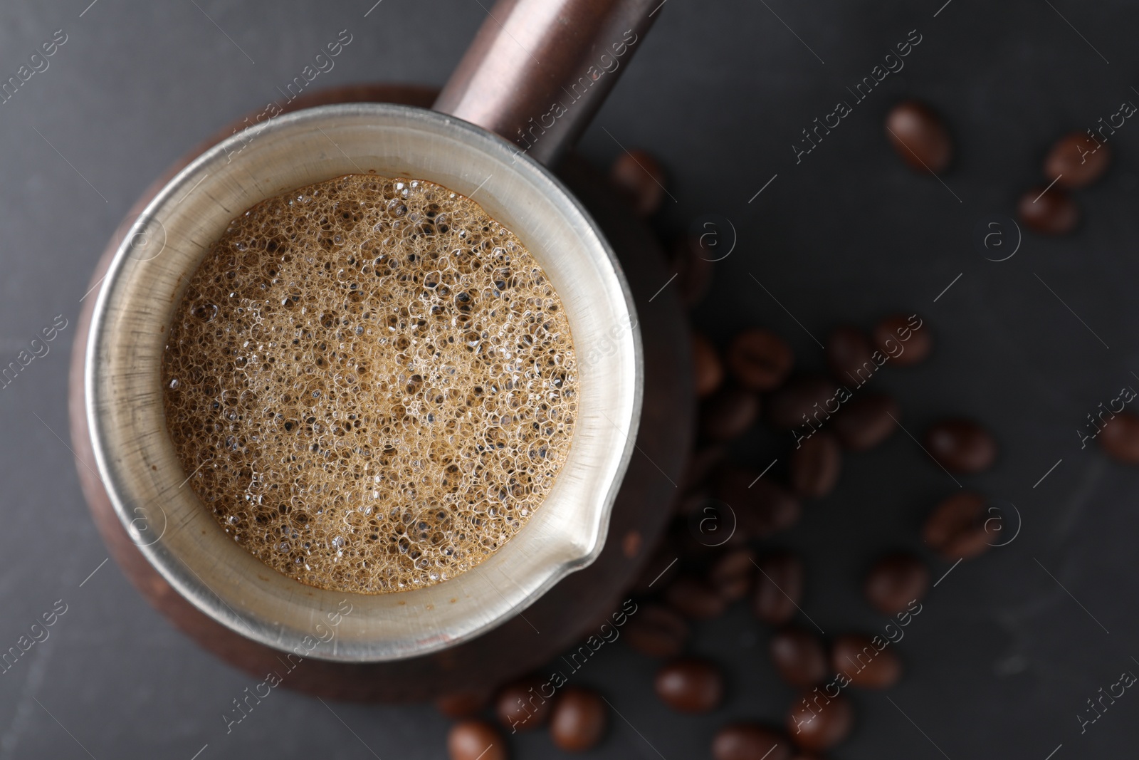 Photo of Cezve with Turkish coffee and beans on dark grey table, top view. Space for text