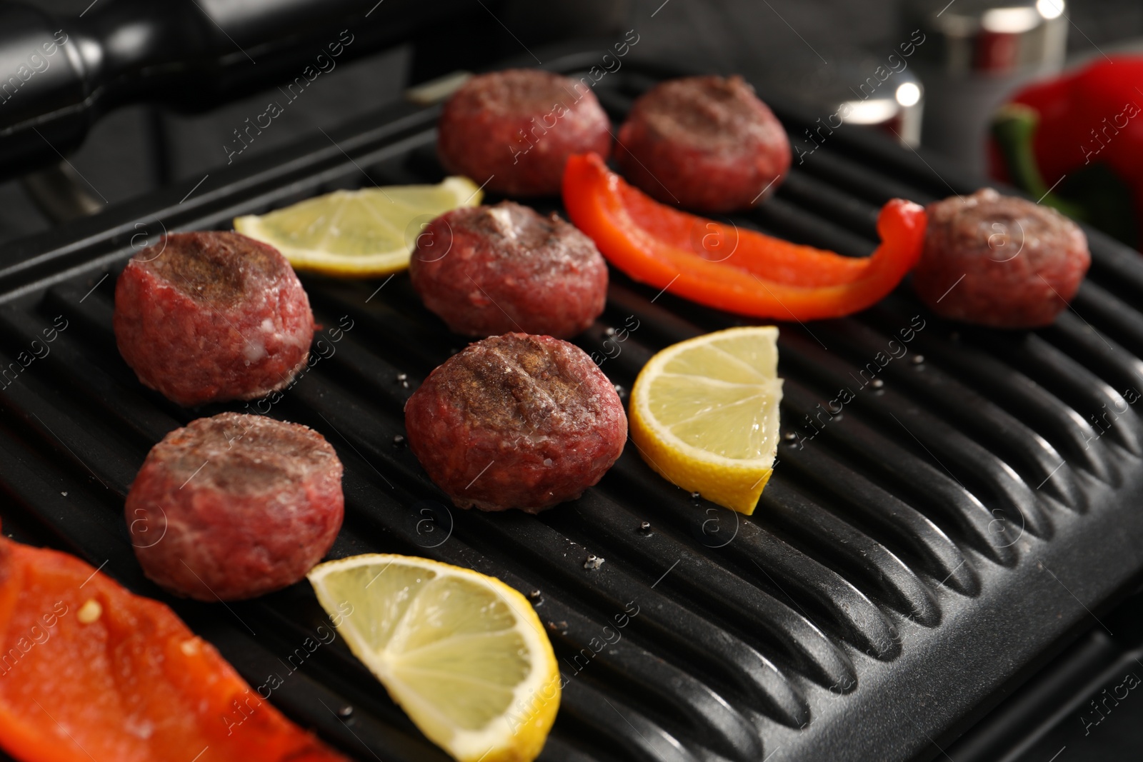 Photo of Electric grill with meat balls, bell pepper and lemon on table, closeup