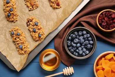 Photo of Making granola bars. Baking tray and ingredients on blue wooden table, flat lay