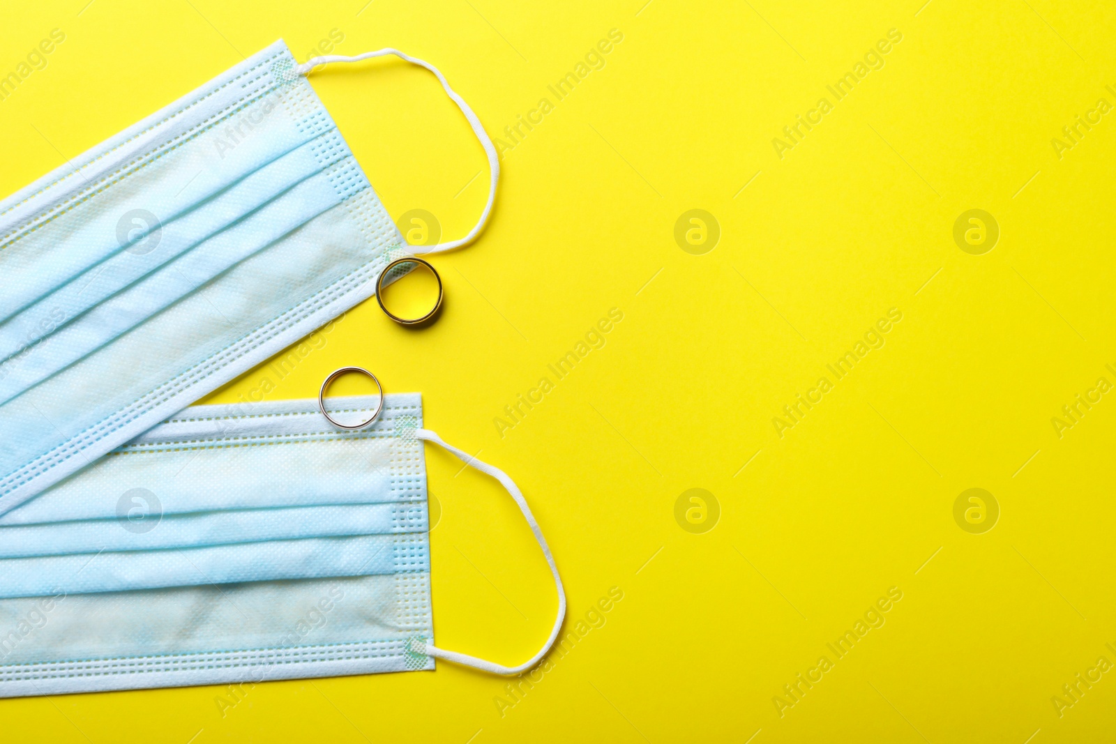 Photo of Protective masks and wedding rings on yellow background, flat lay with space for text. Divorce during coronavirus quarantine
