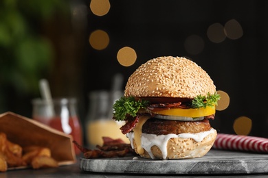 Photo of Fresh juicy bacon burger on board against blurred background. Space for text