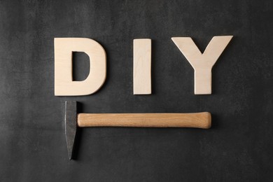 Photo of Abbreviation DIY made of wooden letters and hammer on dark background, flat lay