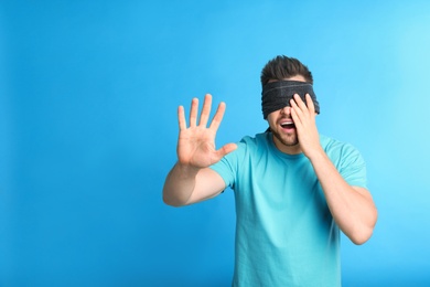 Man with black blindfold on blue background, space for text