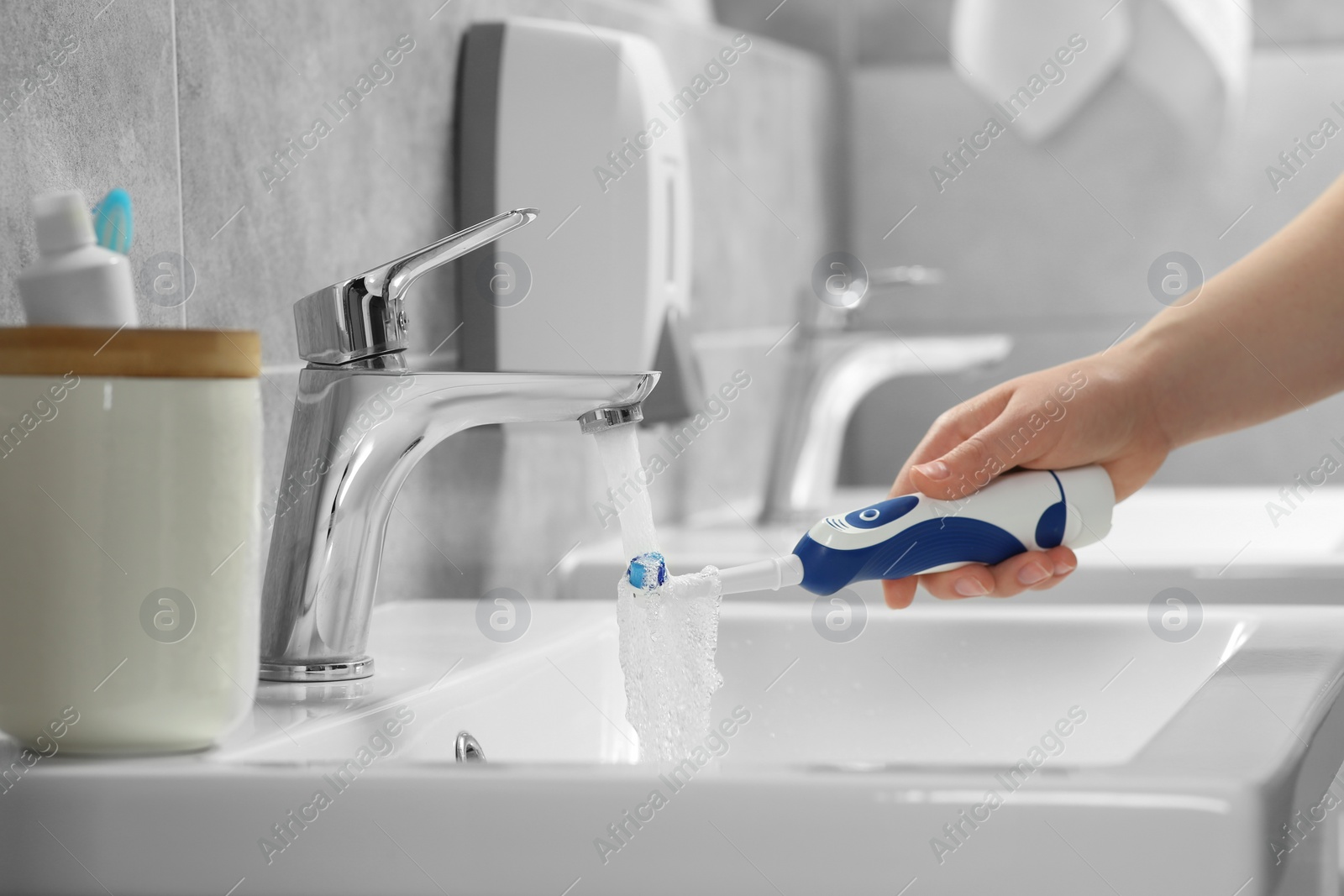 Photo of Woman washing electric toothbrush under flowing water from faucet in bathroom, closeup