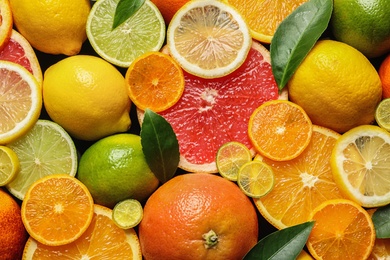 Sliced and whole citrus fruits with leaves as background, top view