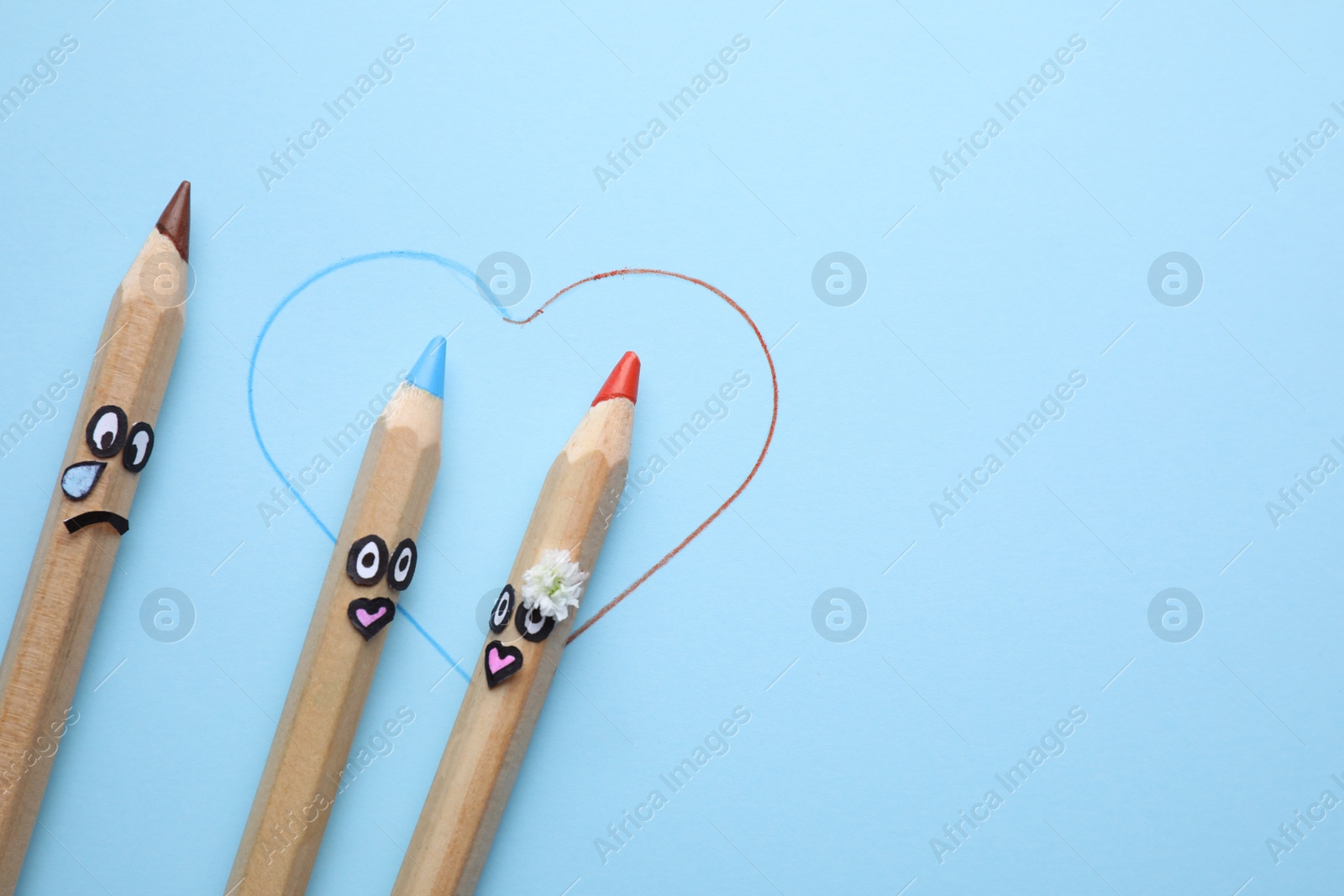 Photo of Pencils with drawn faces on light blue background, flat lay. Concept of jealousy