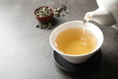 Photo of Pouring green tea into cup on grey table. Space for text