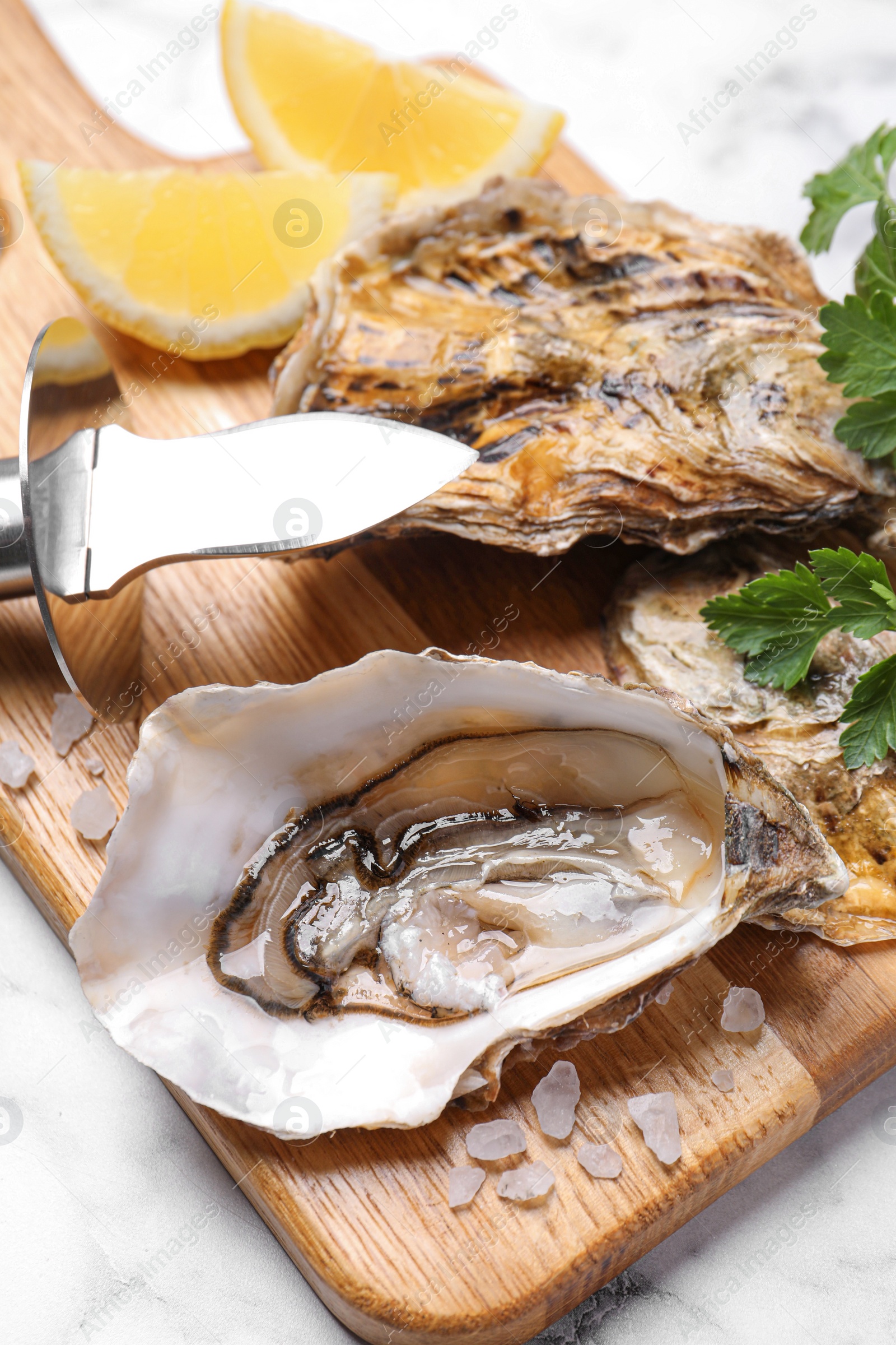 Photo of Fresh oysters with lemon, parsley and knife on white marble table, closeup