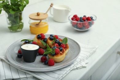 Photo of Delicious cottage cheese pancakes with fresh berries, mint and sour cream on white table. Space for text