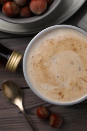 Photo of Mug of delicious coffee with hazelnut syrup on wooden table, flat lay