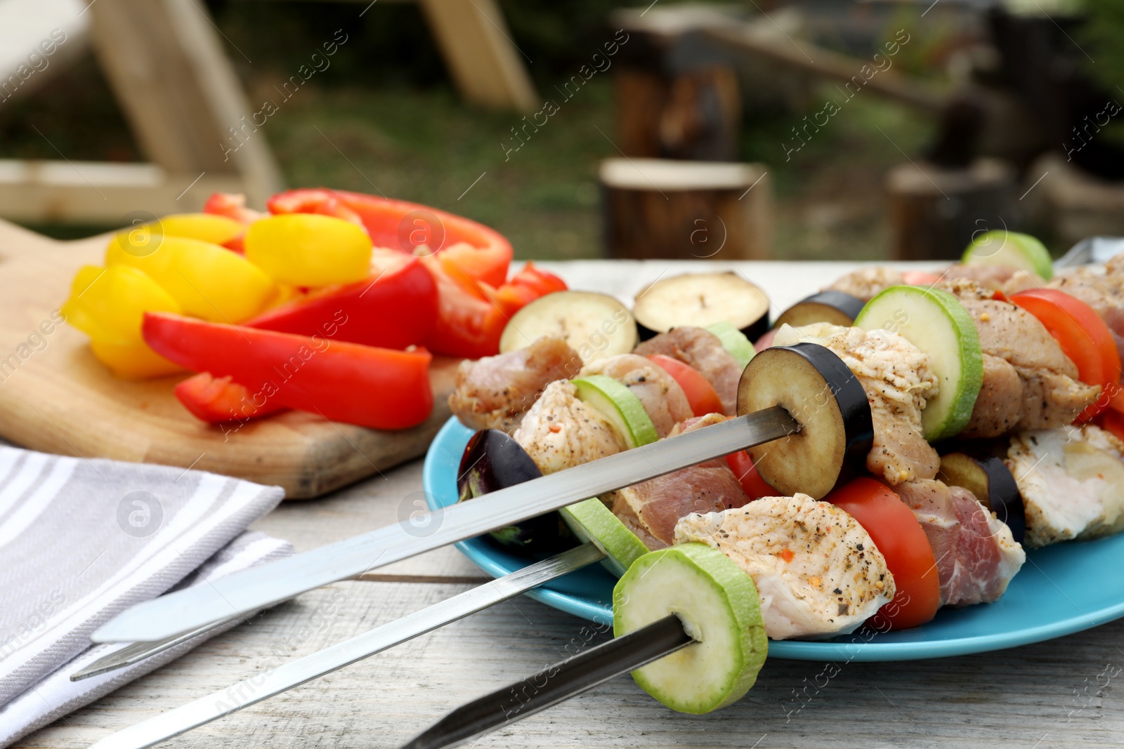 Photo of Metal skewers with raw marinated meat and vegetables on wooden table outdoors