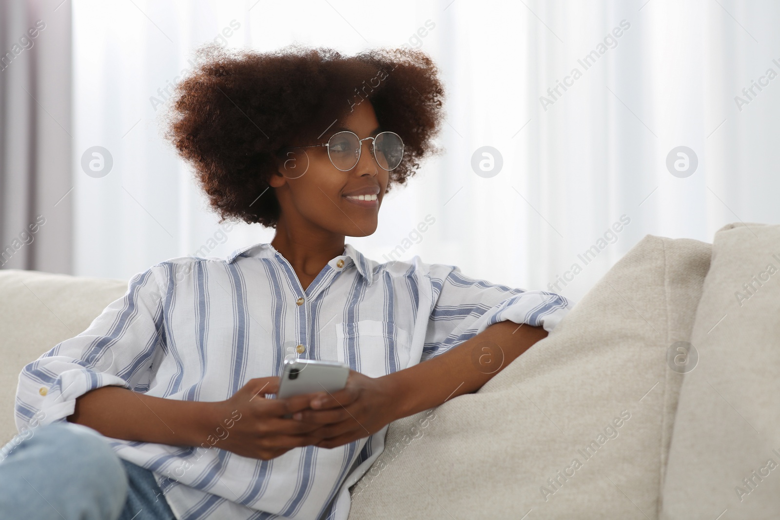 Photo of Smiling African American woman wearing glasses with smartphone at home. Space for text