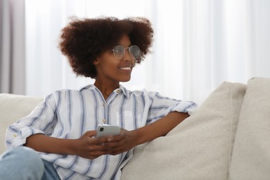 Smiling African American woman wearing glasses with smartphone at home. Space for text