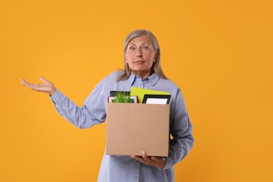 Photo of Confused unemployed senior woman with box of personal office belongings on orange background