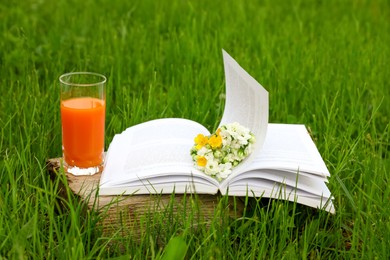 Photo of Open book with flowers and glass of juice on green grass outdoors