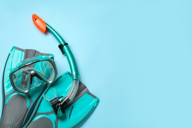 Photo of Pair of turquoise flippers and mask on light blue background, flat lay. Space for text