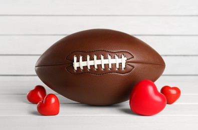 Photo of American football ball and hearts on white wooden table