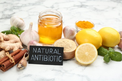 Photo of Different fresh products and card with phrase Natural Antibiotic on white marble table