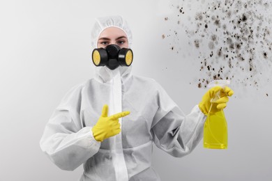 Image of Woman in protective suit and rubber gloves pointing at mold remover near affected wall