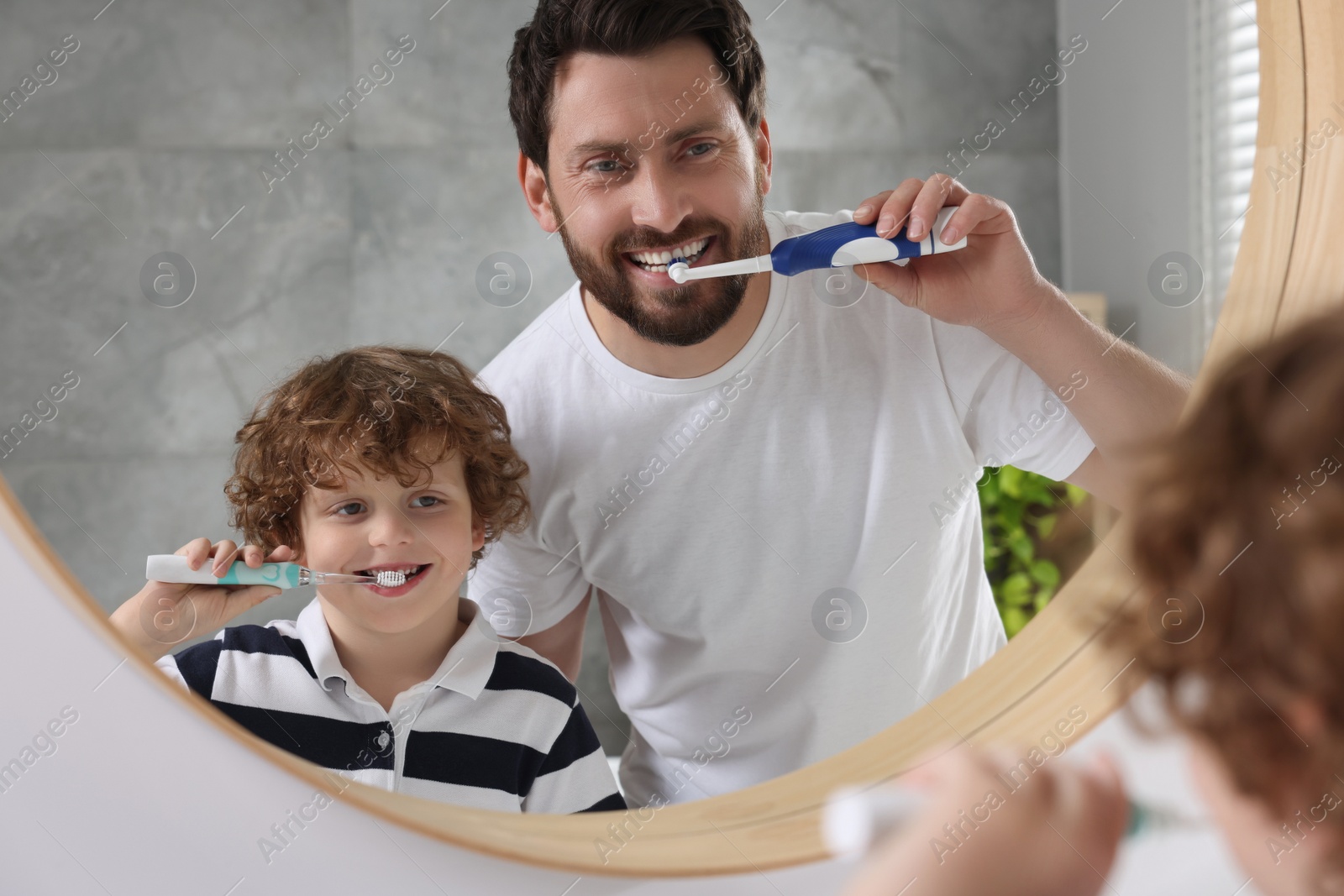 Photo of Father and his son brushing teeth together near mirror indoors