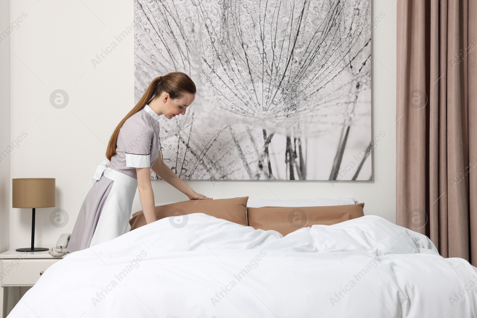 Photo of Young maid making bed in hotel room. Space for text