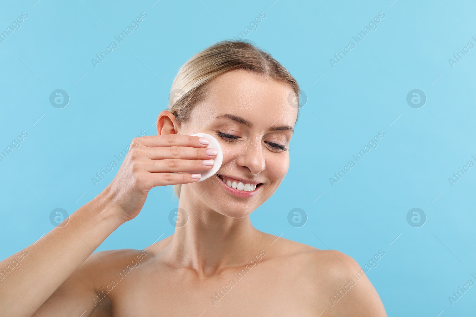 Photo of Smiling woman removing makeup with cotton pad on light blue background