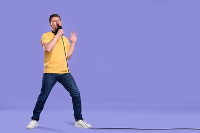 Photo of Handsome man with microphone singing on violet background. Space for text