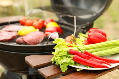 Plate with vegetables near barbecue grill outdoors, closeup