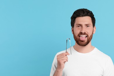 Happy man with tongue cleaner on light blue background, space for text